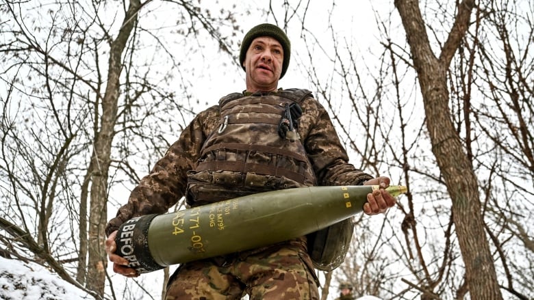 Soldier in camo holds a shell in a snowy forest