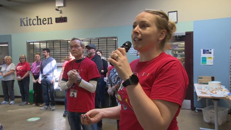 A woman is seen speaking into a microphone in front of a row of people lined up.