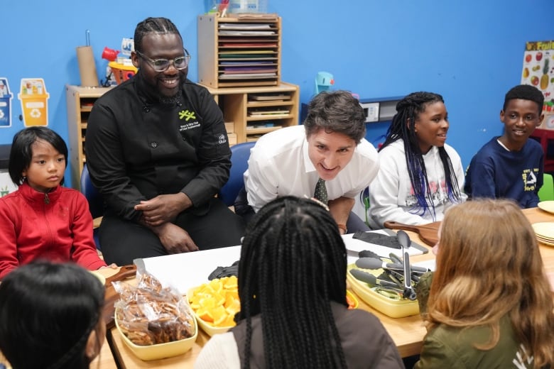 A  man in a suit sits at  a table with diverse children in  a colourful room