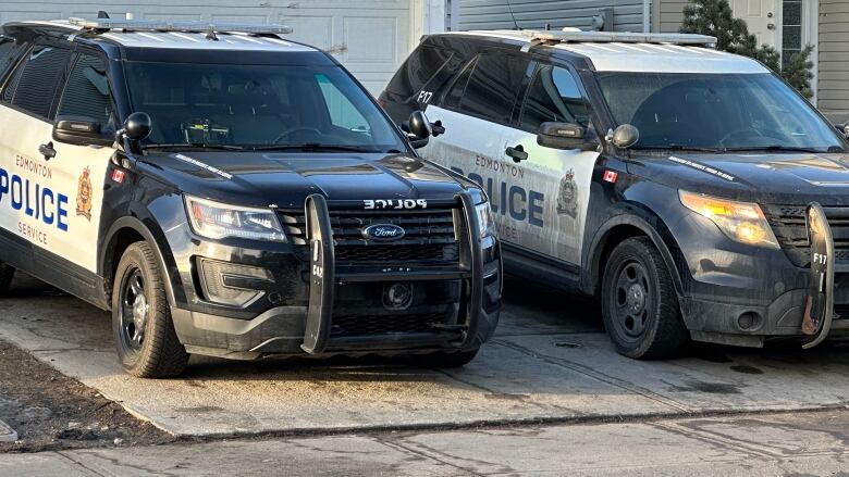 Two marked police cruisers backed into a driveway in front of a home.