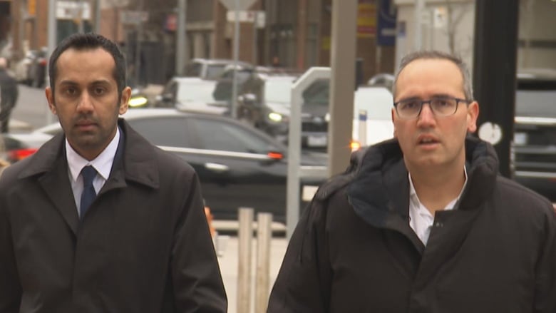 Two men in coats walking on sidewalk.