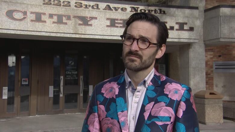 A man in a floral blazer stands outside city hall