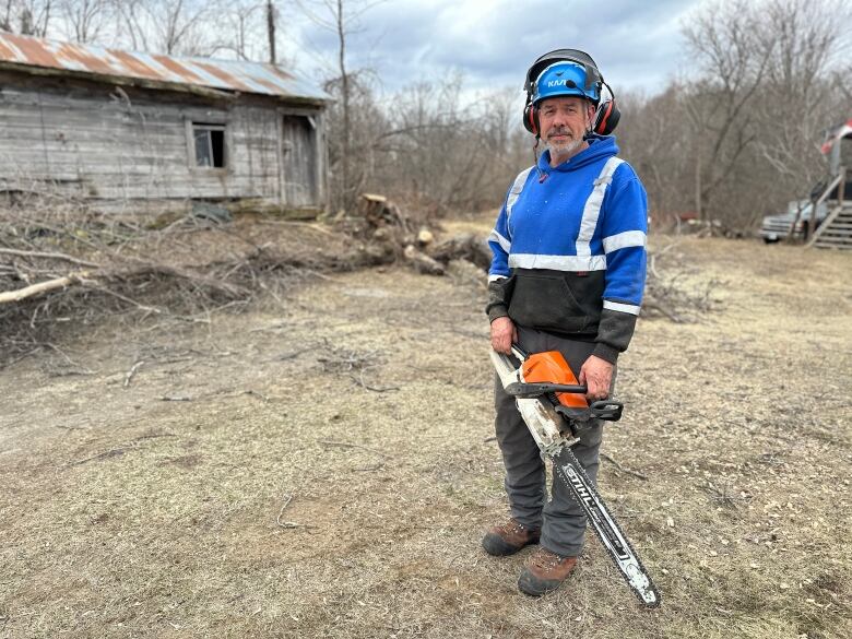 A worker holds a chainsaw next to a felled tree in early spring.