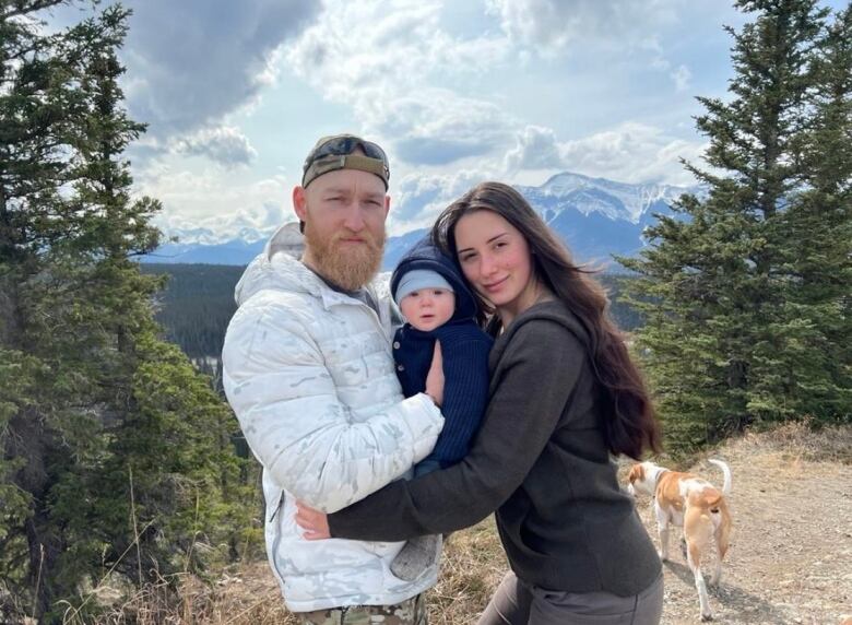 a woman with a baby in a carrier and a man with a light beard sit for an outdoor portrait