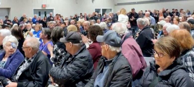 People sit in rows of chairs in a large community centre space