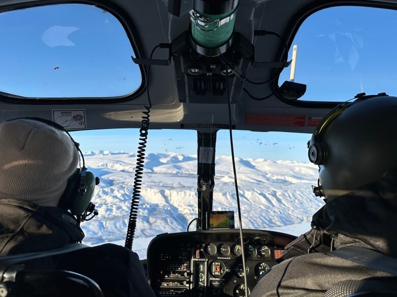 Two people flying in a helicopter, seen from the back. 