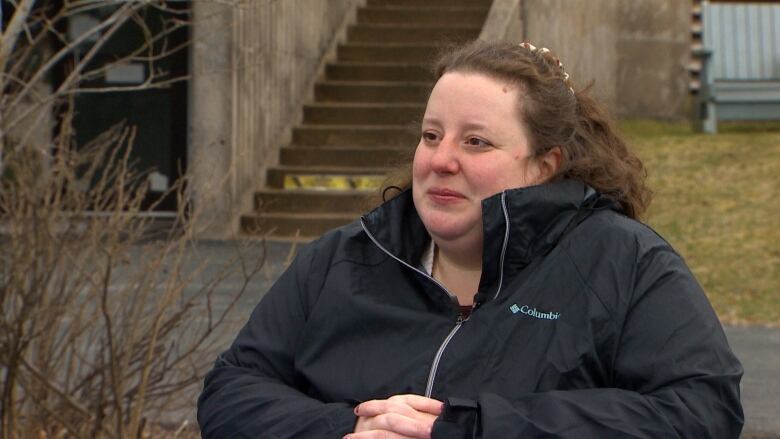 A woman sits outside. She is wearing a black Columbia raincoat and has her light brown hair tied back. 