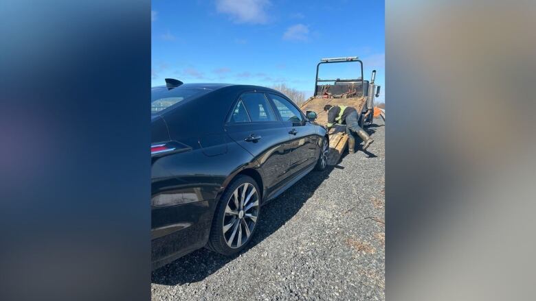 A tow truck pulls a black car on to its bed on a clear day.