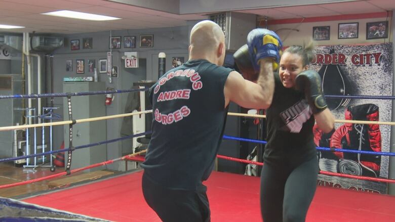 A teenage female boxer hits pads held by a coach in a ring.