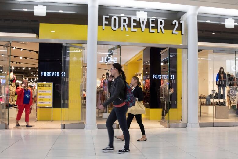 Shoppers talk on their phones while walking in a mall by a store with a sign that says Forever 21.