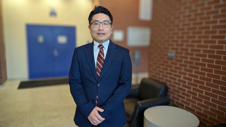 A man in a suit and tie stands in a university hallway 