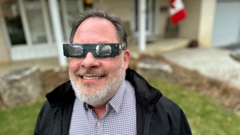 man stands outside house wearing safety eclipse glasses