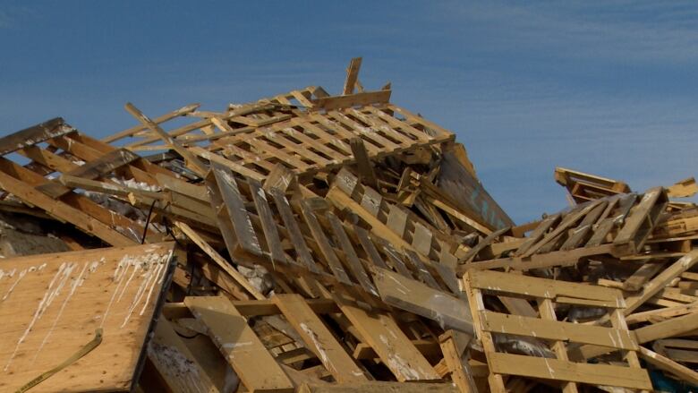 A big pile of wood pallets with a clear blue sky in the background.