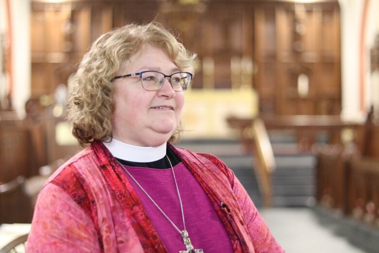 A woman in Bishop's clothing is facing the right and smiling. She is standing inside a cathedral.