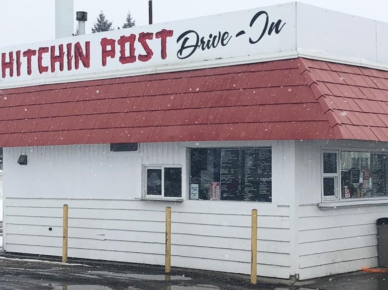 A photo of a drive-in eatery that has the words, Hitchin' Post Drive-In displayed at the front of the restaurant.