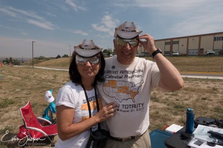 A couple smiles at the camera wearing eclipse glasses.