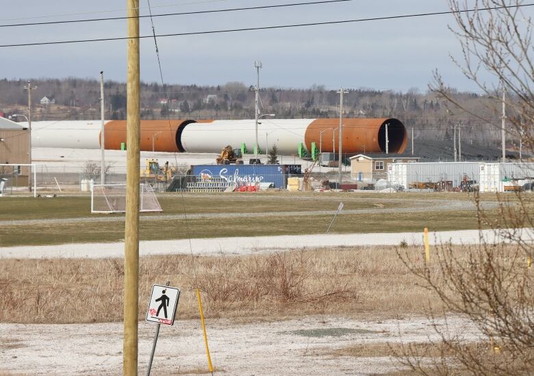 Several large grey-and-rust-coloured steel tubes lie on their sides dwarfing nearby buildings and a shipping container.