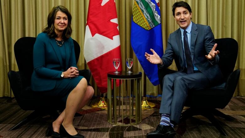 a woman on the left and a man on the right sit in two chairs and smile for cameras