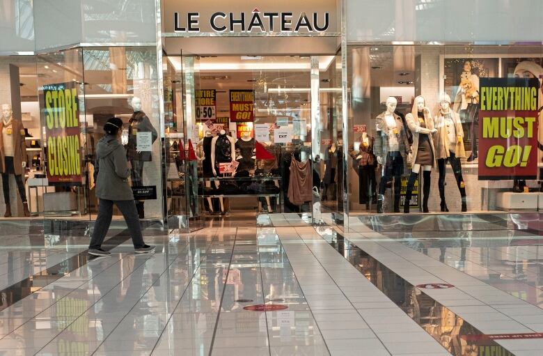 A woman in a face mask walks past Le Chateau, a clothing store, which has 