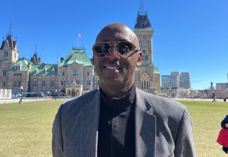 A man wearing sunglasses stands outside. 