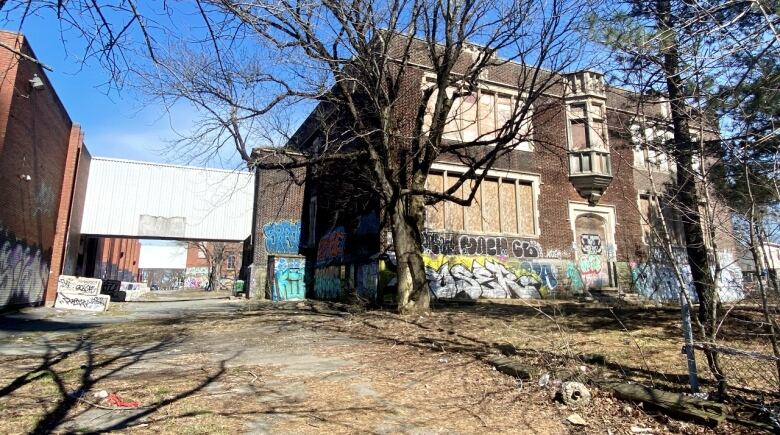 A dark brown brick building stands back from the road with bare trees in front of it. There's a white pedway attaching it to a larger red brick building on the left