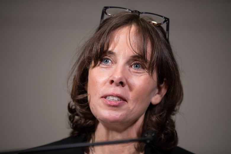 A white woman with black hair and glasses atop her head speaks.