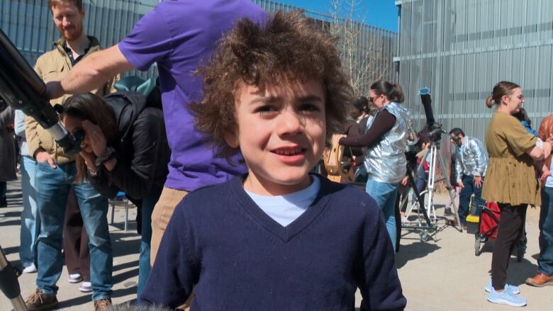 A boy in a sweater smiles at the camera. 