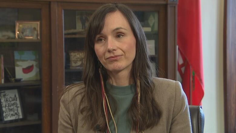 A woman with long, brown hair is pictured. She's wearing a suit and sits looking forward.