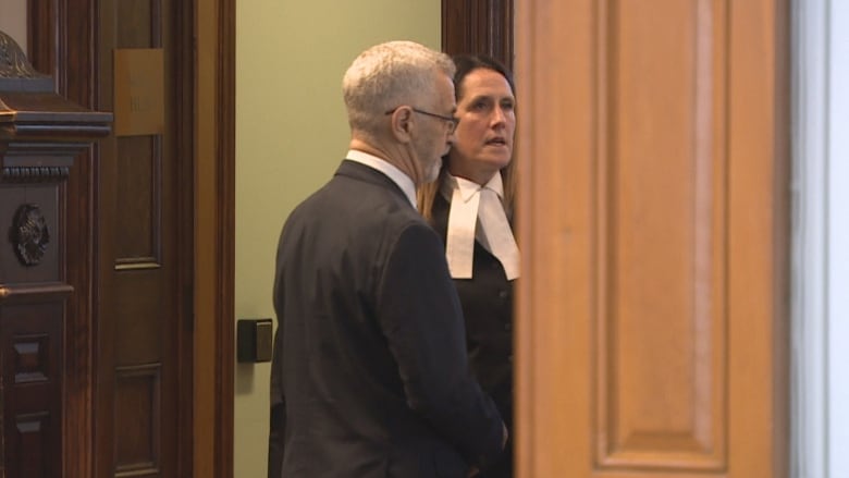 A woman in a black robe with a white neck tie speaks with a greyhaired man in a suit. 