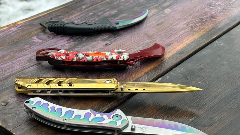 Four pocket-sized knives, purchased by community members, sit on a picnic table. 