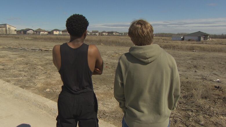 Two teen boys are pictured from behind, looking at an open stretch of grass in front of them.