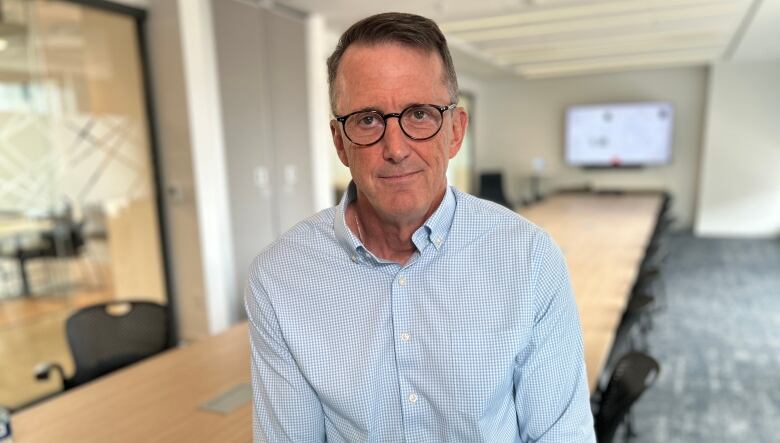 A man in a light blue dress shirt standing in front of a boardroom table.