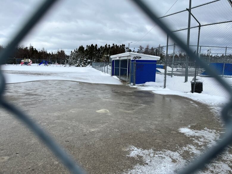 a photo of a snow- and ice-covered baseball field, framed through chain linked fencing.