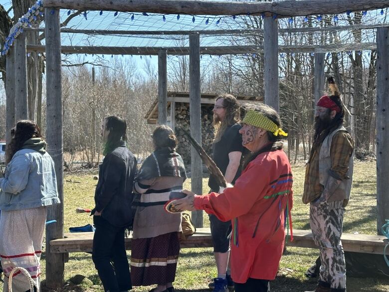 A group of people stand outside in a circle of wooden posts facing the same direction.