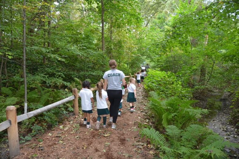 Girls walk on a path through the woods, accompanied by a woman with the word 