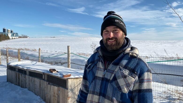 White man with beard wearing blue plaid winter jacket and black tuque standing outside during winter.