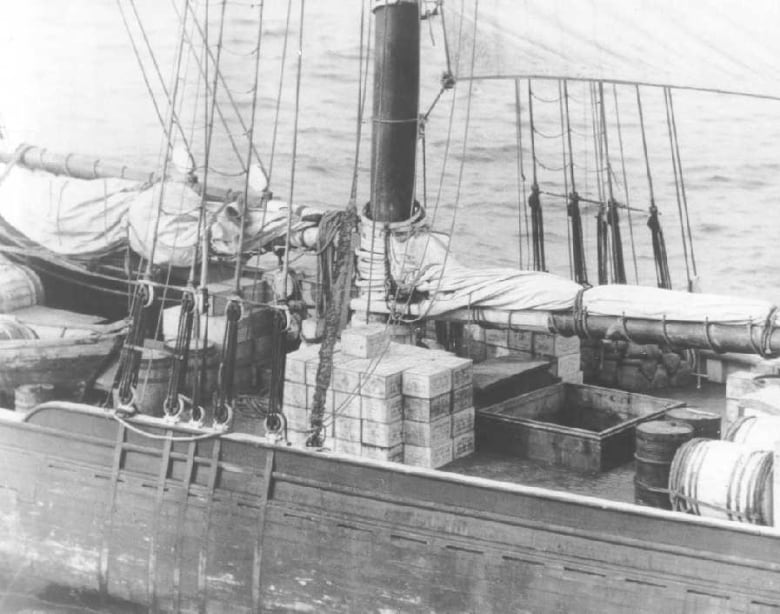 A black and white photo of the deck of a wooden ship with boxes of cargo visible.