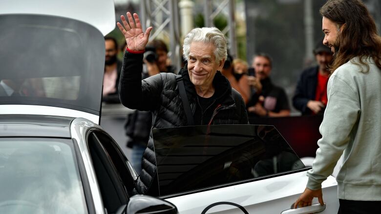 A man waves at a crowd while he exits a car. 