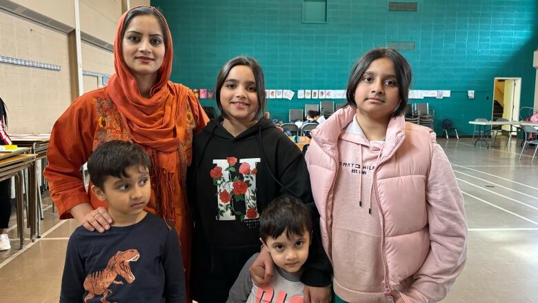 A woman wearing a hijab stands with her four young children. 