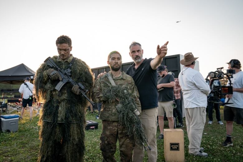 Alex Garland is seen on set of the movie Civil War along with two men in army fatigues.