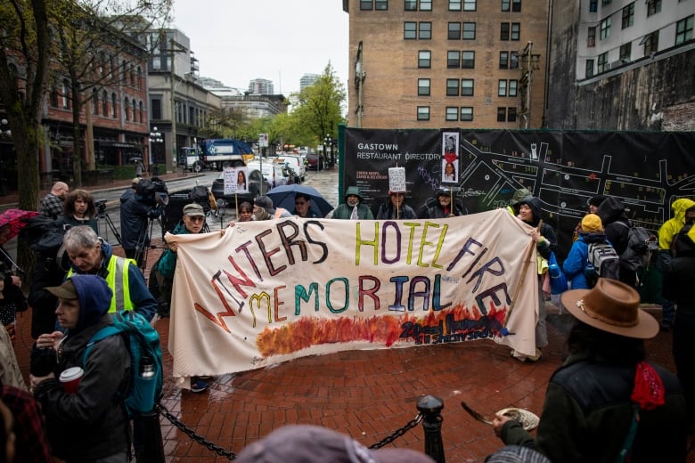 People gathered in a street holding a banner, which says Winter Hotel Fire Memorial