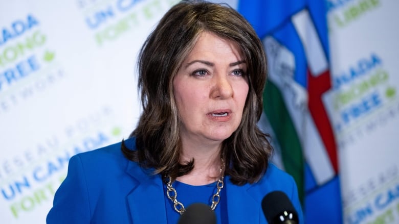 a woman in a blue suit speaks at a microphone