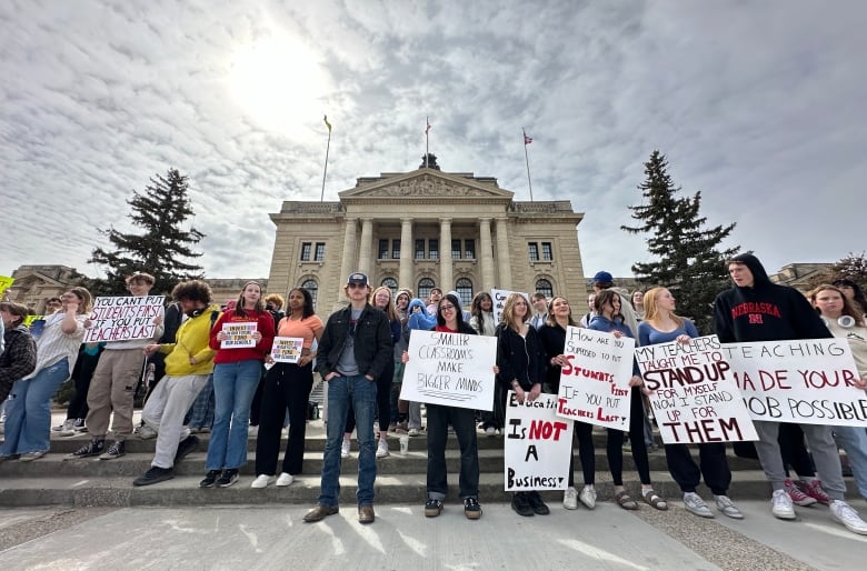 A group of young people hold signs while standing in front of a marble-columned building. 