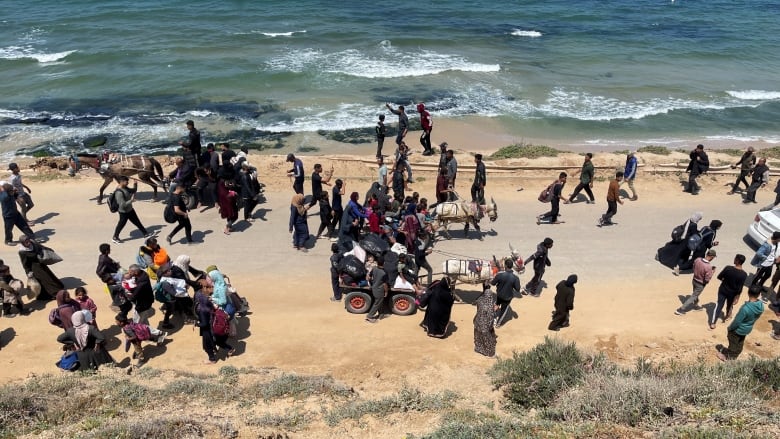 People carry their belongings as they walk along a road near a body of water.