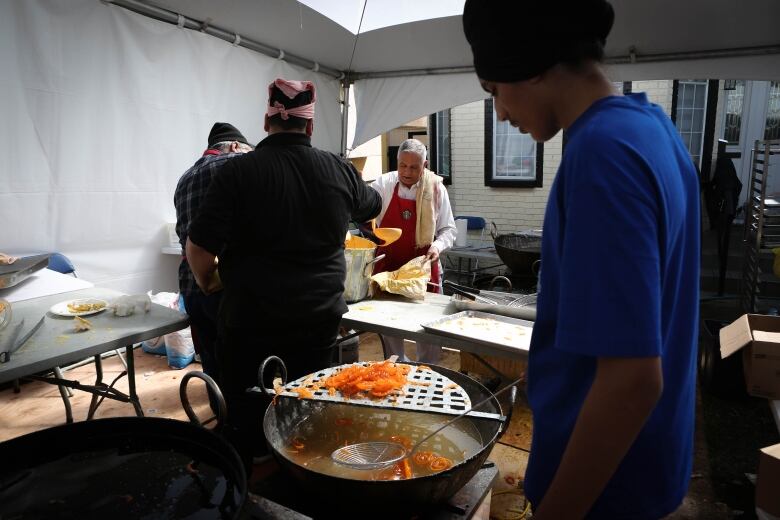 A turbaned man fries sweets in a large vessel, as others hand out plates.