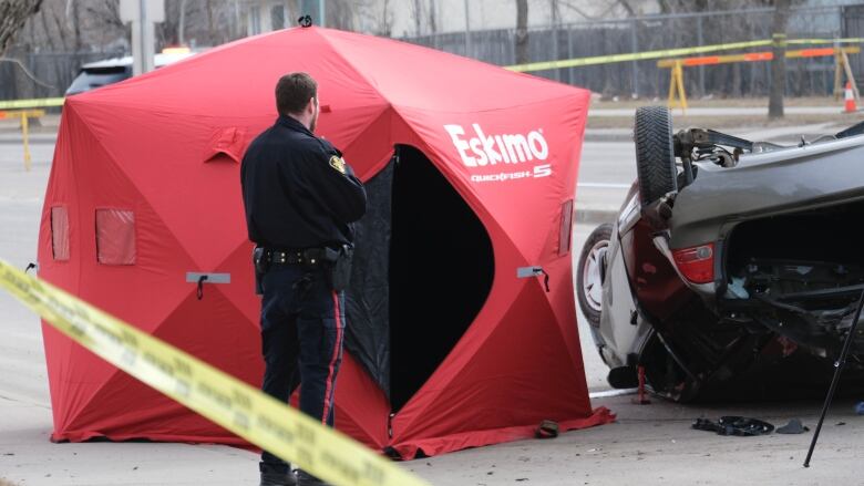 A Saskatoon Police Service officer is beside an upside down vehicle with a red tent popped up beside it