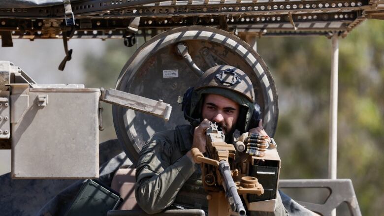 A mustached soldier is shown peaking out atop a tank-like military vehicle in a daytime photo.