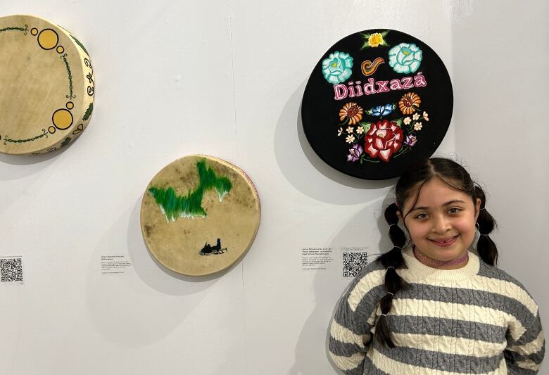 Girl standing next to a drum hanging on the wall