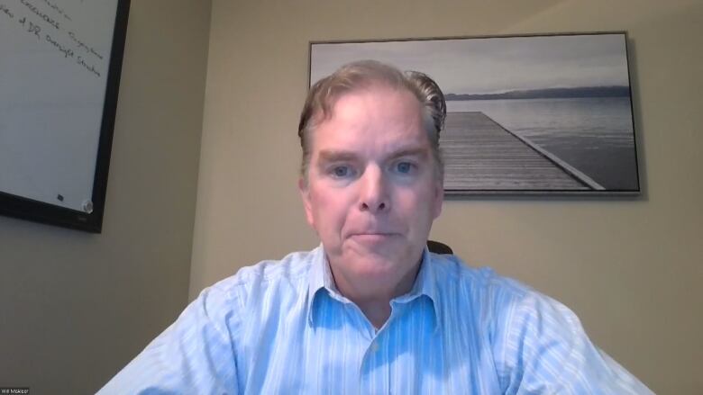 Will McAleer is wearing a light blue pinstriped collared shirt. He's sitting in front of a picture of a dock floating in a body of water.