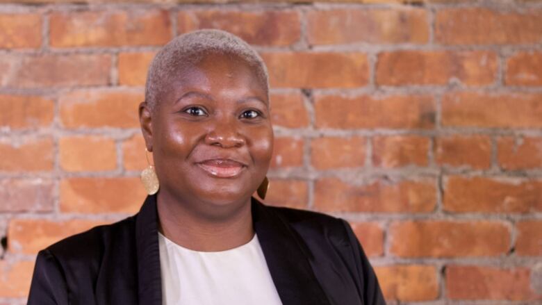 A portrait of a woman in a blazer standing against a brick wall.